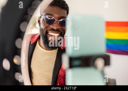 Persona felice non-binaria che indossa gli occhiali da sole e fa il vlog a casa Foto Stock