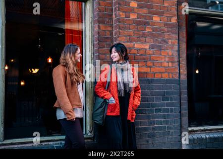 Sorelle felici in piedi e che parlano vicino al muro Foto Stock