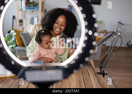 Madre e figlia felici con microfono davanti alla luce anulare illuminata a casa Foto Stock