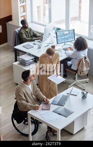 Manager che si prende l'aiuto di un professionista IT seduto in sedia a rotelle alla reception Foto Stock