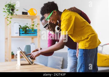 Ragazzo felice che insegna al nonno a usare un tablet PC a casa Foto Stock
