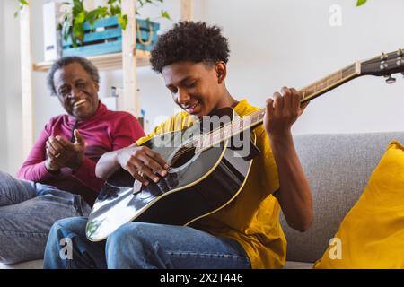 Ragazzo sorridente che suona la chitarra di nonno sul divano di casa Foto Stock