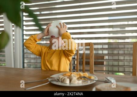 Ragazzo che beve latte dalla ciotola seduto a tavola a casa Foto Stock