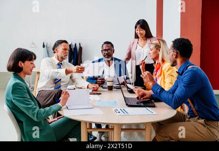 Uomo d'affari che mostra un documento ai colleghi seduti alla scrivania in ufficio Foto Stock
