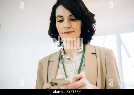 Donna d'affari matura e sicura di sé che utilizza lo smartphone in ufficio Foto Stock