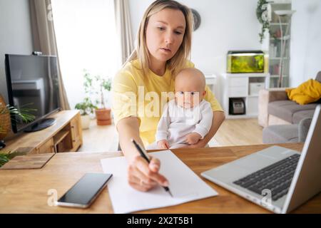 Donna d'affari che scrive su carta seduta con un figlio a tavola Foto Stock
