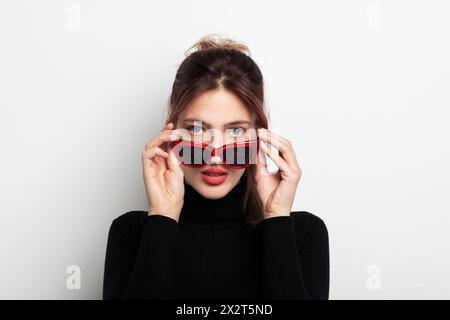 Bella giovane donna che indossa occhiali da sole su sfondo bianco Foto Stock