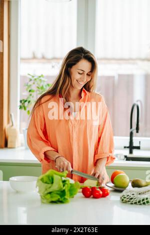 Donna sorridente che trita verdure in cucina a casa Foto Stock