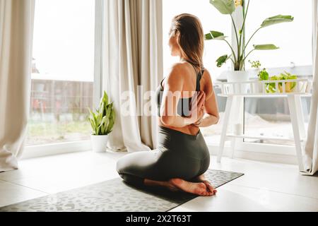 Donna che fa posa di preghiera inversa sul tappetino da yoga a casa Foto Stock