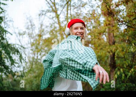 Giovane donna felice che ascolta la musica con le cuffie wireless e balla davanti agli alberi Foto Stock