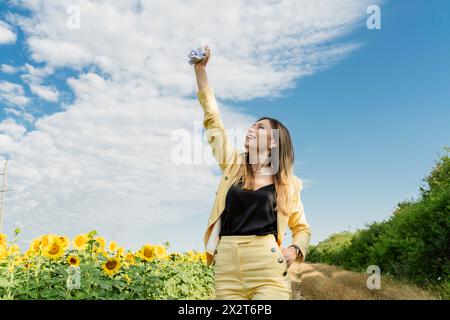 Donna d'affari spensierata che tiene la carta in grembo in piedi nel campo dei girasoli Foto Stock