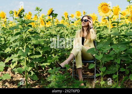 Donna d'affari sorridente seduta su una sedia tra girasoli nel campo Foto Stock