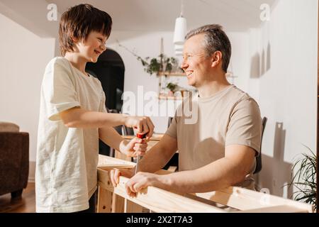 Felice figlio e padre che usano un cacciavite su mobili in legno a casa Foto Stock