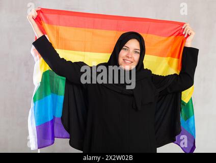 Felice giovane donna vestita con abiti tradizionali islamici con bandiera arcobaleno Foto Stock