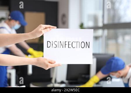 Lavoratore di servizio di pulizia che tiene la carta con la DISINFEZIONE parola in ufficio, primo piano Foto Stock