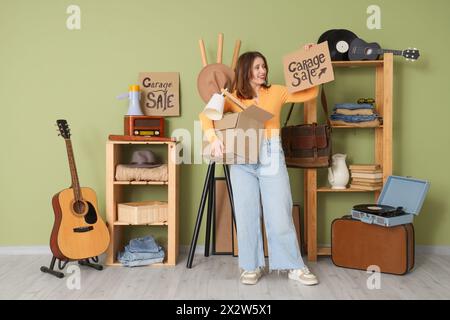Giovane donna che tiene in mano cartone con VENDITA DI GARAGE e scatola in camera di oggetti indesiderati Foto Stock