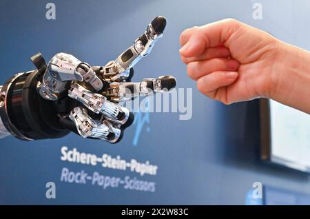 Hannover, Germania. 23 aprile 2024. Un visitatore gioca a forbici da carta rock con un robot intelligente alla Hannover Messe di Hannover, Germania, il 23 aprile 2024. La fiera Hannover Messe 2024, la fiera industriale leader in Germania, ha dato il via lunedì con una chiara enfasi sulla produzione a emissioni zero e sulle celle a combustibile a idrogeno. Crediti: Ren Pengfei/Xinhua/Alamy Live News Foto Stock