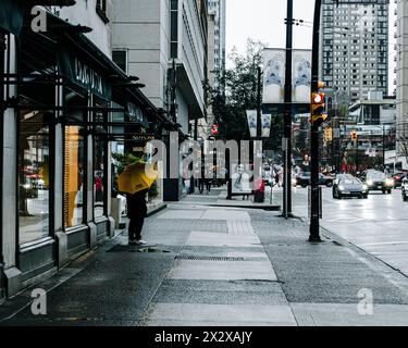 Vancouver, Canada - febbraio 28 2024: Una persona con un ombrello giallo è in piedi sul lato del marciapiede di Burrard Street. Quell'uomo sta guardando verso Foto Stock