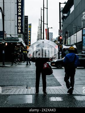 Vancouver, Canada - febbraio 28 2024: Un uomo che tiene in mano un ombrello trasparente e un borsone in attesa di attraversare Georgia Street in una mattina piovosa Foto Stock