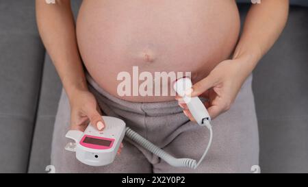 Primo piano della pancia di una donna incinta usando un doppler domestico. Schermo vuoto. Foto Stock