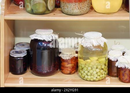 Vasetti grandi e piccoli con marmellata, funghi stufati e sottaceto sono sugli scaffali. Foto Stock
