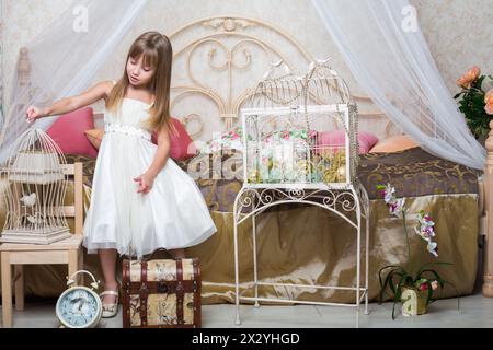 Bambina in camera da letto che tiene una gabbia con un uccello Foto Stock