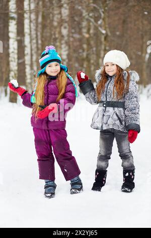 Due amiche sorridenti si trovano nel parco invernale, pronte a lanciare palle di neve Foto Stock