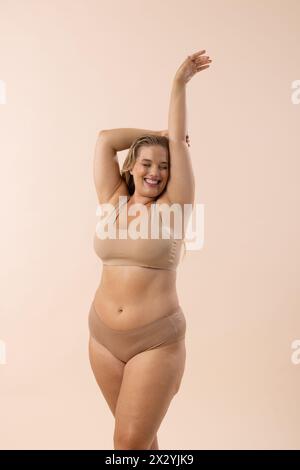 Il modello caucasico Plus-size in beige si pone su sfondo coordinato, spazio copia Foto Stock