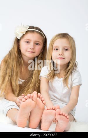 Due bambine vestite di bianco sedute sulla pelliccia Foto Stock