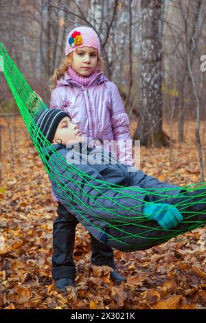 Un ragazzo con sua sorella che si rilassa in un'amaca nella foresta autunnale Foto Stock