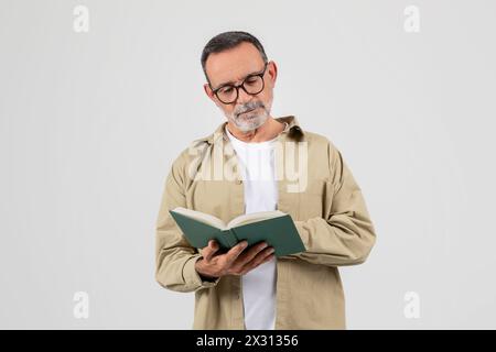 Uomo con barba e occhiali che legge un libro Foto Stock