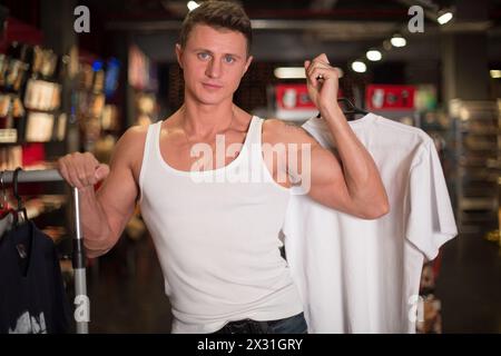 Un uomo con un giubbotto bianco sceglie i vestiti in negozio Foto Stock