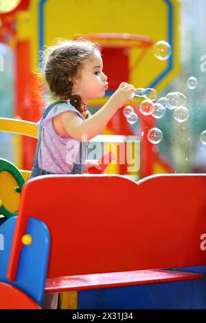 Una bambina che soffia molte bolle di sapone nel parco giochi Foto Stock