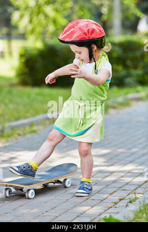 La bambina con il casco protettivo impara a fare skateboard nel parco Foto Stock