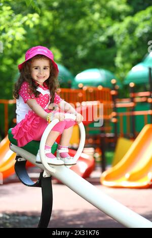 Ritratto di una bambina sorridente in un cappello rosa seduta su un'altalena Foto Stock