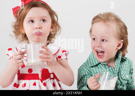 Bambino e bambina con un vestito brillante che bevono latte da tazze di vetro Foto Stock