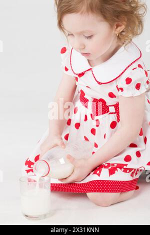 Bambina con un abito a pois che versa latte da una biberon in una tazza Foto Stock