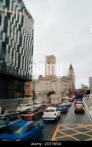 Vista sfocata del traffico stradale di Liverpool in una giornata di pioggia attraverso il finestrino a goccia di pioggia di un autobus a due piani Foto Stock