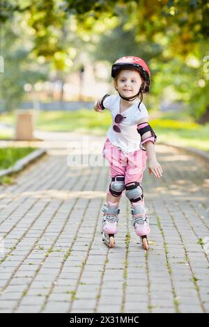 Bambina in attrezzatura protettiva pattini a rotelle sul passaggio pedonale nel parco Foto Stock