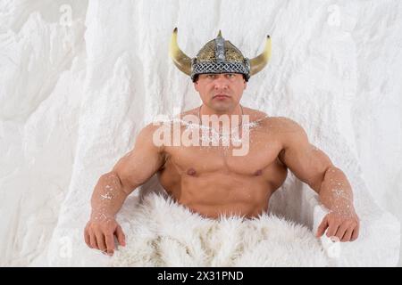 Un uomo muscoloso in un casco vichingo con neve sul corpo e pelliccia Foto Stock