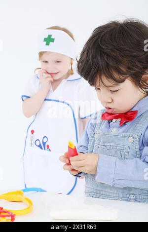 Il bambino gioca con strumenti medici giocattolo e la ragazza lo guarda su sfondo bianco. Concentrati sul ragazzo. Foto Stock