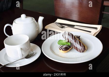 Eclari con crema ricoperta di cioccolato su un piatto e tè nel caffè Foto Stock