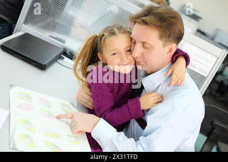 La figlia felice abbraccia suo padre che guarda il libretto di appartamenti in ufficio. Concentrati sulle ragazze. Foto Stock