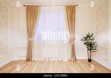 Finestra con tende beige in camera semplice con pianta al piano nel nuovo appartamento. Foto Stock
