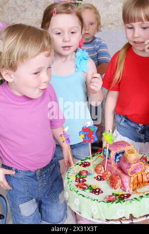 Il ragazzo di compleanno fa saltare le candele sulla torta e tre suoi amici lo guardano alla festa dei bambini. Foto Stock