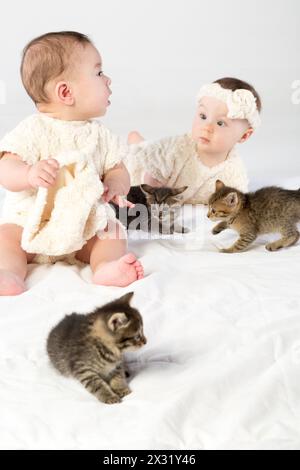 Due bambini vestiti in pelliccia bianca giocano con i piccoli gattini Foto Stock