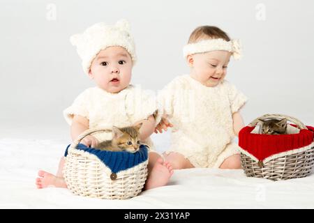 Due bimbi vestiti in pelliccia bianca con due cesti con gattini piccoli Foto Stock