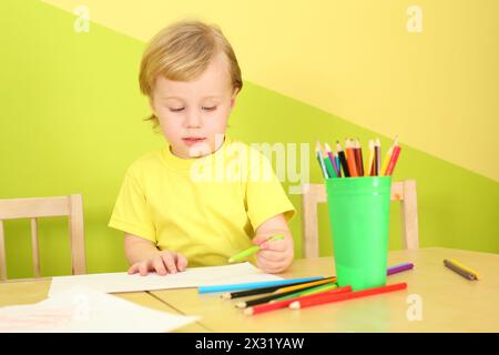 Il bambino disegna con matite colorate sedute a un tavolo in una stanza luminosa Foto Stock