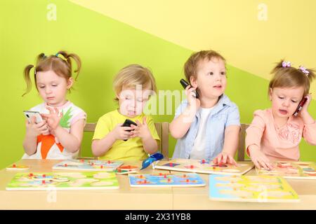 Due ragazzi e due ragazze con il telefono in mano sono seduti a un tavolo con i giocattoli Foto Stock