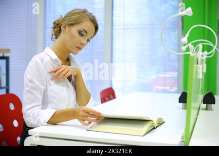 Una bella ragazza sfoglia un libro in biblioteca Foto Stock
